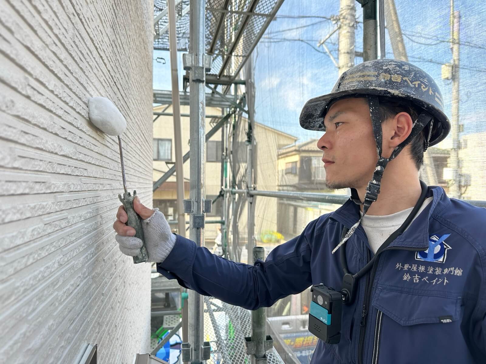 足場の上で外壁をローラー塗装する職人